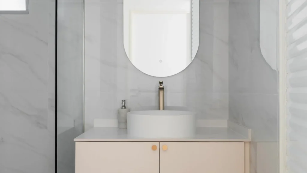 Floating vanity with oval mirror and marble walls in HDB bathroom by 6AM Spaces