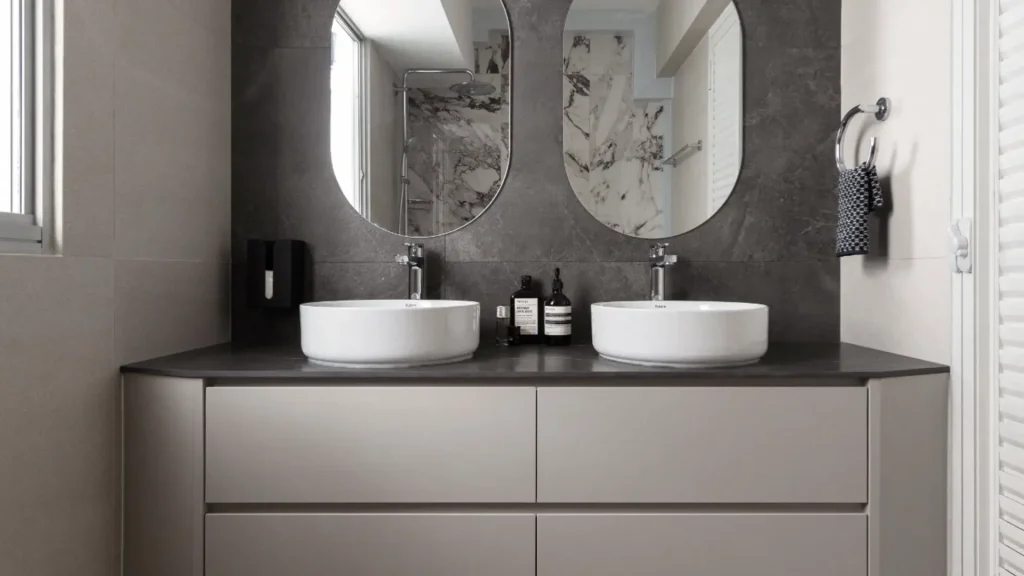 Dual-basin vanity with dark stone feature wall and oval mirrors in HDB bathroom renovation