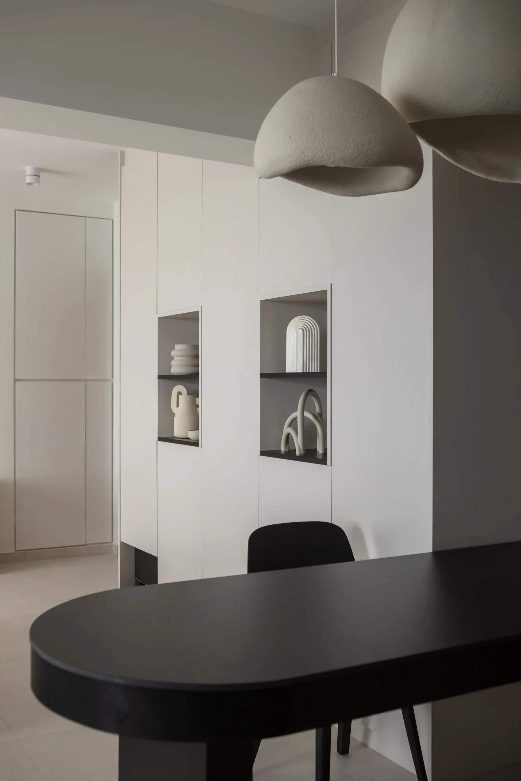 Custom white floor-to-ceiling storage with recessed display niches and organic ceramic decor in a minimalist interior design.