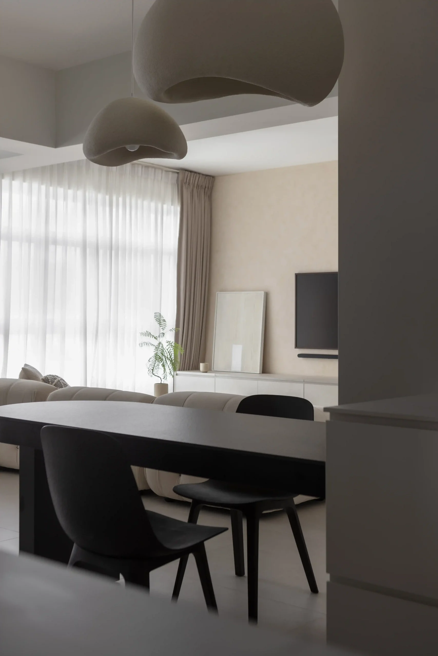 Open-concept living and dining area boasting neutral tones, a black dining table, and large windows with sheer curtains.