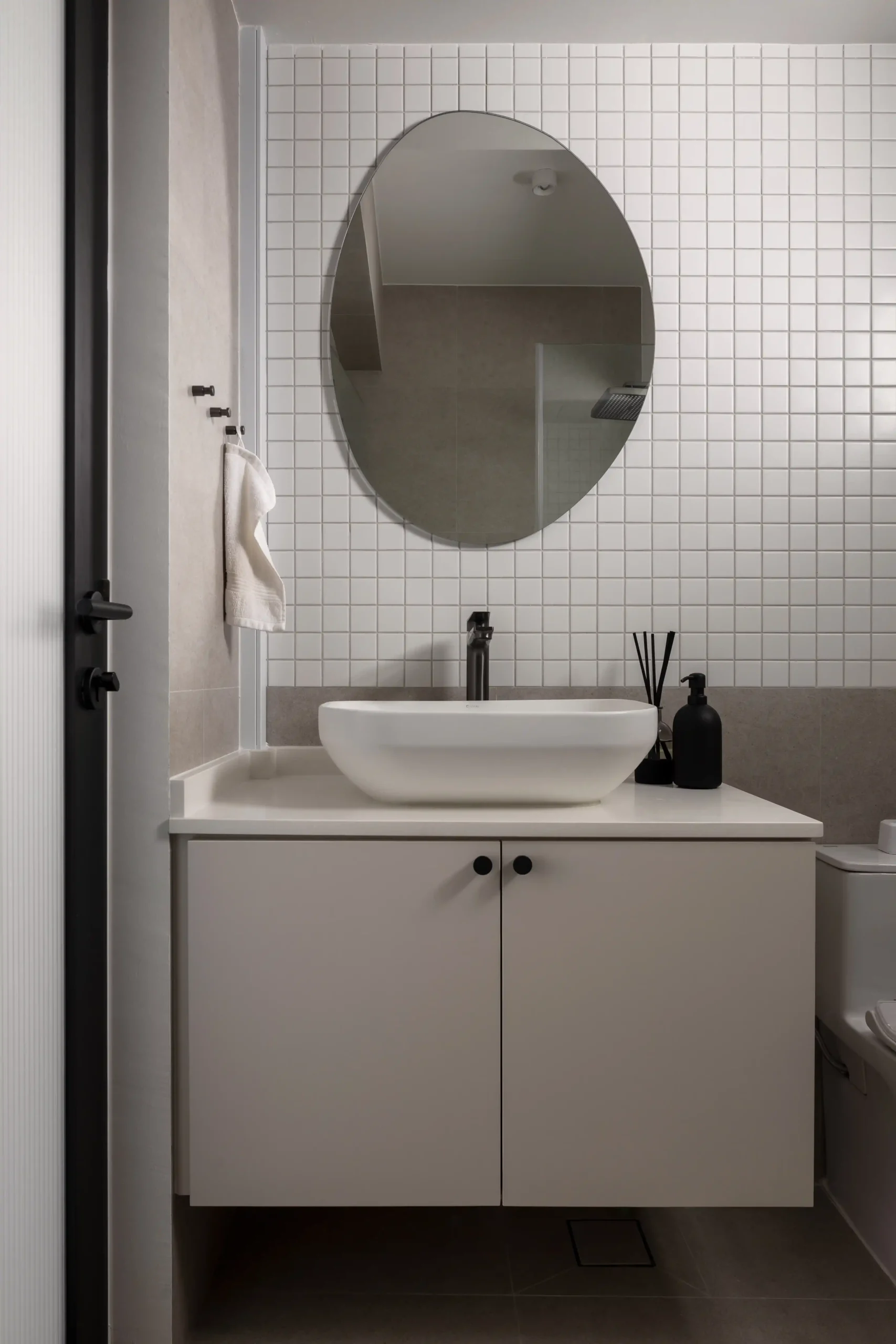Modern bathroom vanity featuring a white vessel sink, floating cabinetry, asymmetric oval mirror, and a square mosaic tile backsplash.