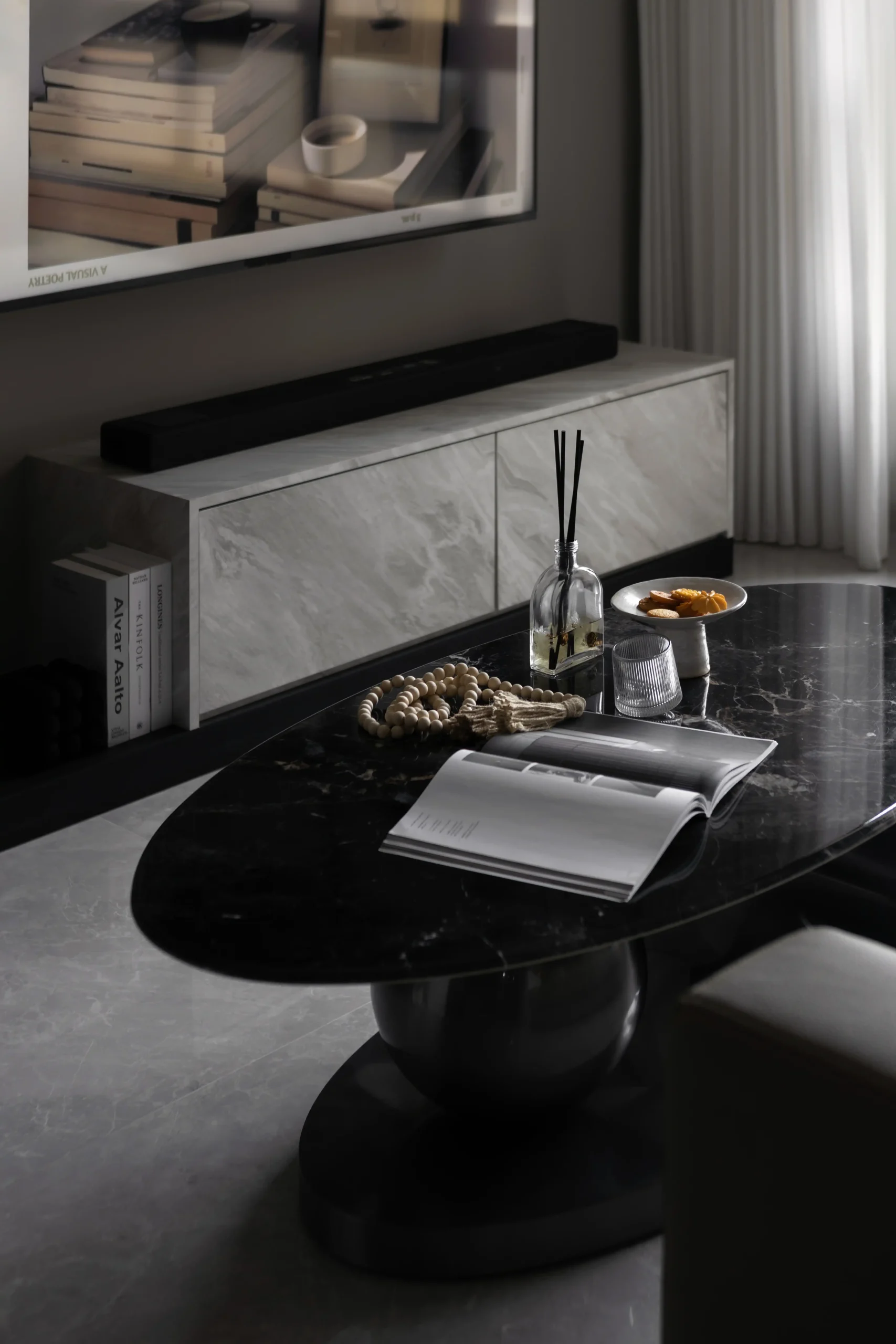 Polished black marble coffee table decorated with books, a glass diffuser, and a white marble media console.
