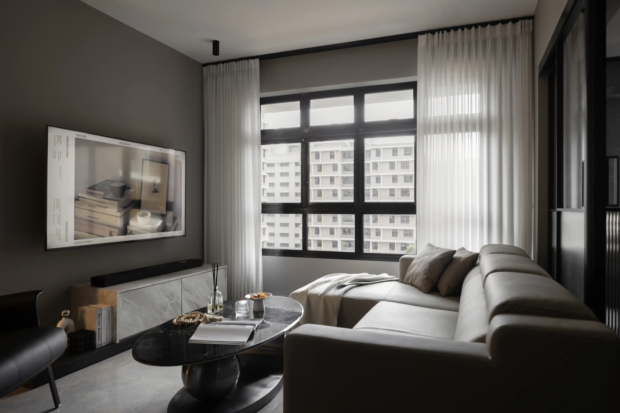 Living space boasting a minimalist gray sofa, dark charcoal walls, and sheer white curtains filtering natural light from a large window.