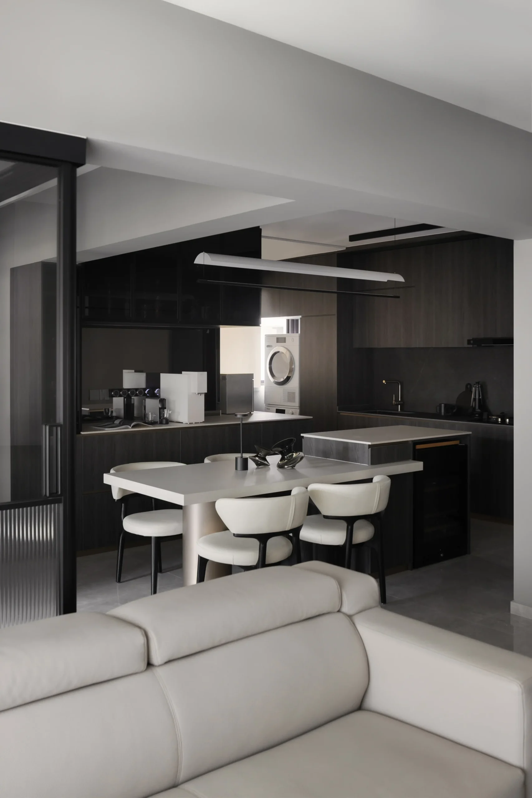 open-concept modern dark luxury interior design kitchen and dining area featuring charcoal wood cabinets, a light gray island table, and structured white chairs.