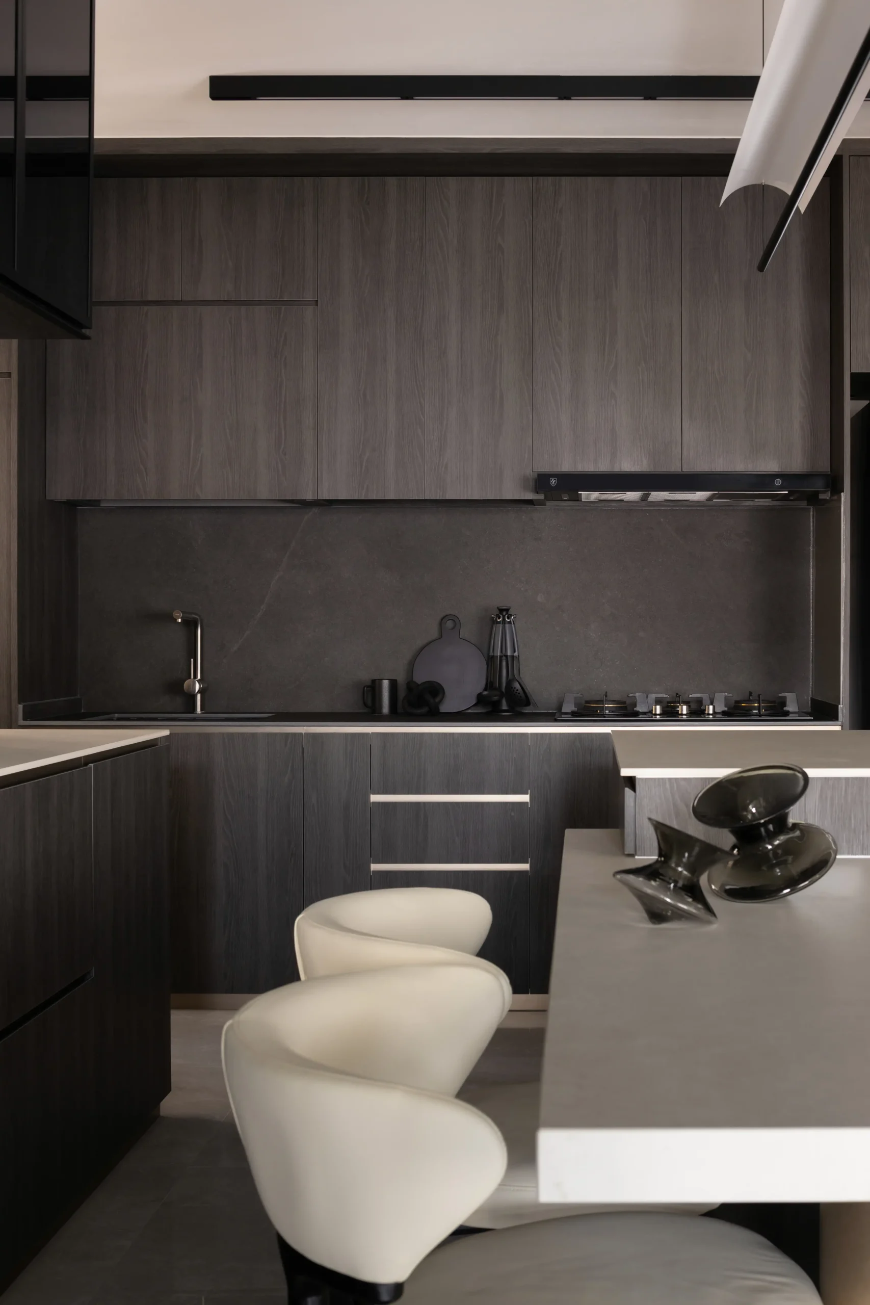 A minimalist moody kitchen backdrop showing seamless dark wood cabinetry, a matte black stone backsplash, and a sleek built-in gas stovetop.