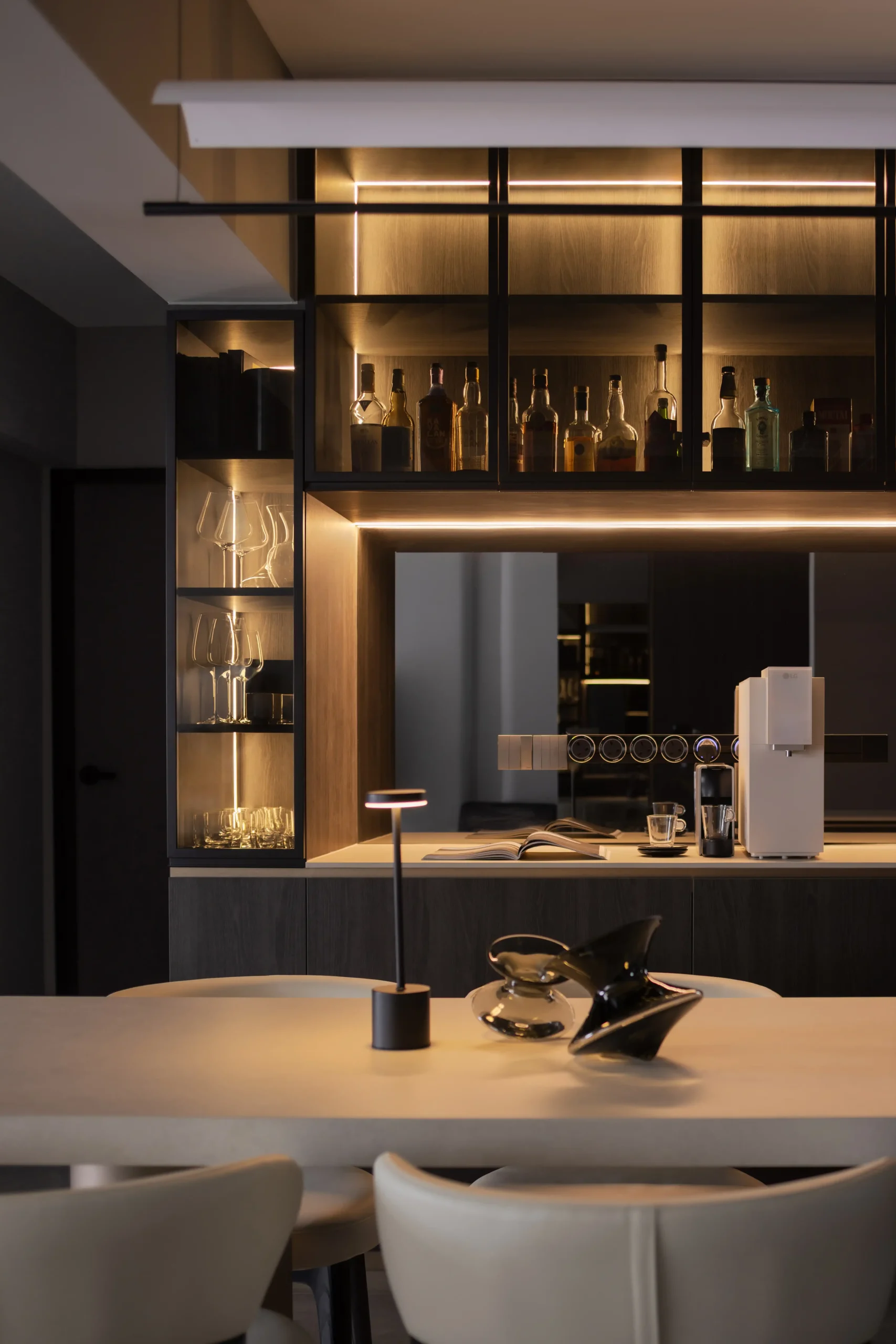 dining space featuring a modern white concrete table with structured white leather chairs beneath a sleek backlit liquor cabinet.