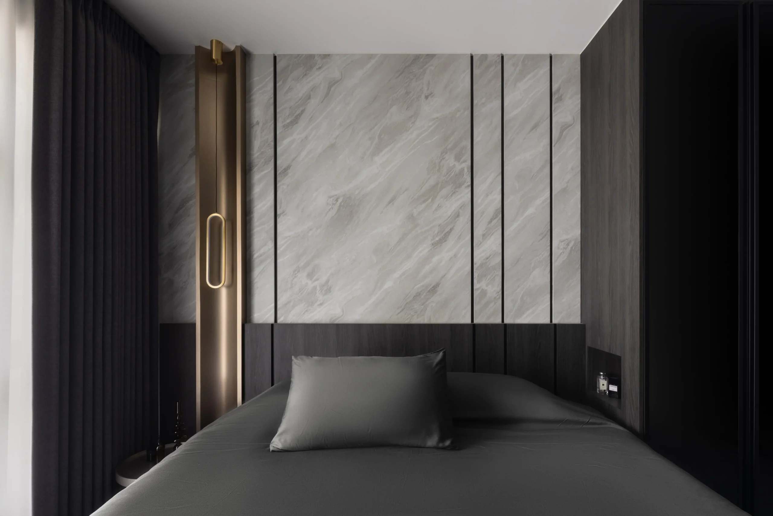 modern bedroom featuring a gray marble slab accent wall, dark wood paneling, and an unlit bronze oval pendant light by the bed