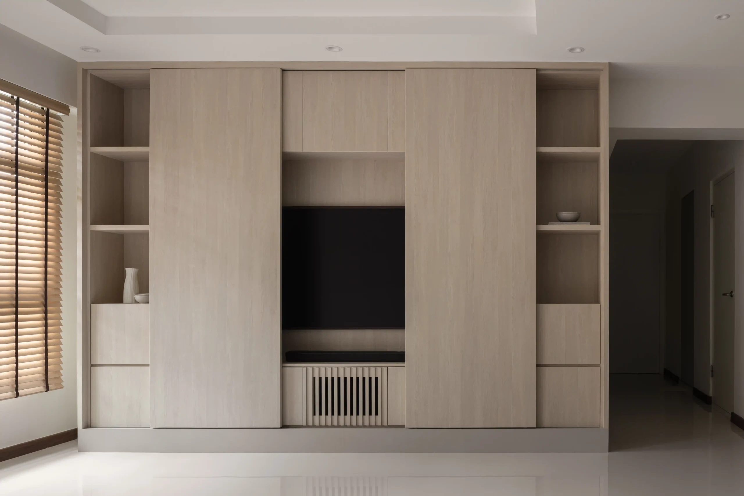 Custom wooden wall unit with open shelves and sliding panels revealing a hidden TV console in a japandi minimalist living space.