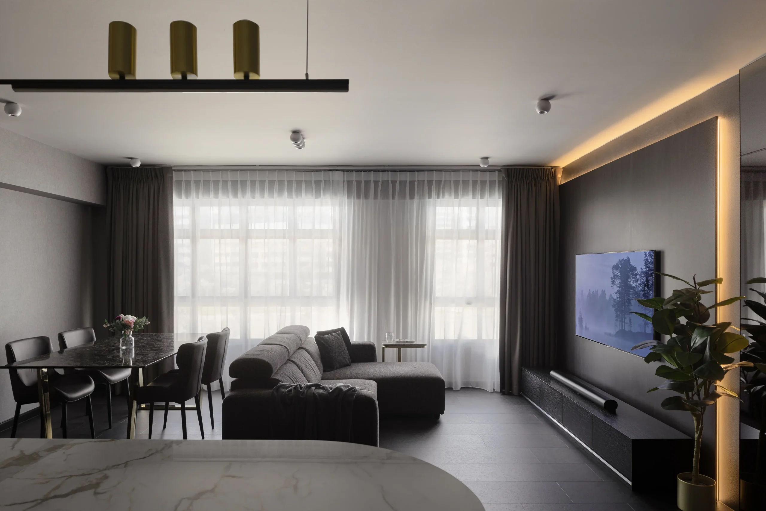 Modern luxury apartment design featuring a dark grey living room, marble dining table, and warm LED backlit TV wall panel.