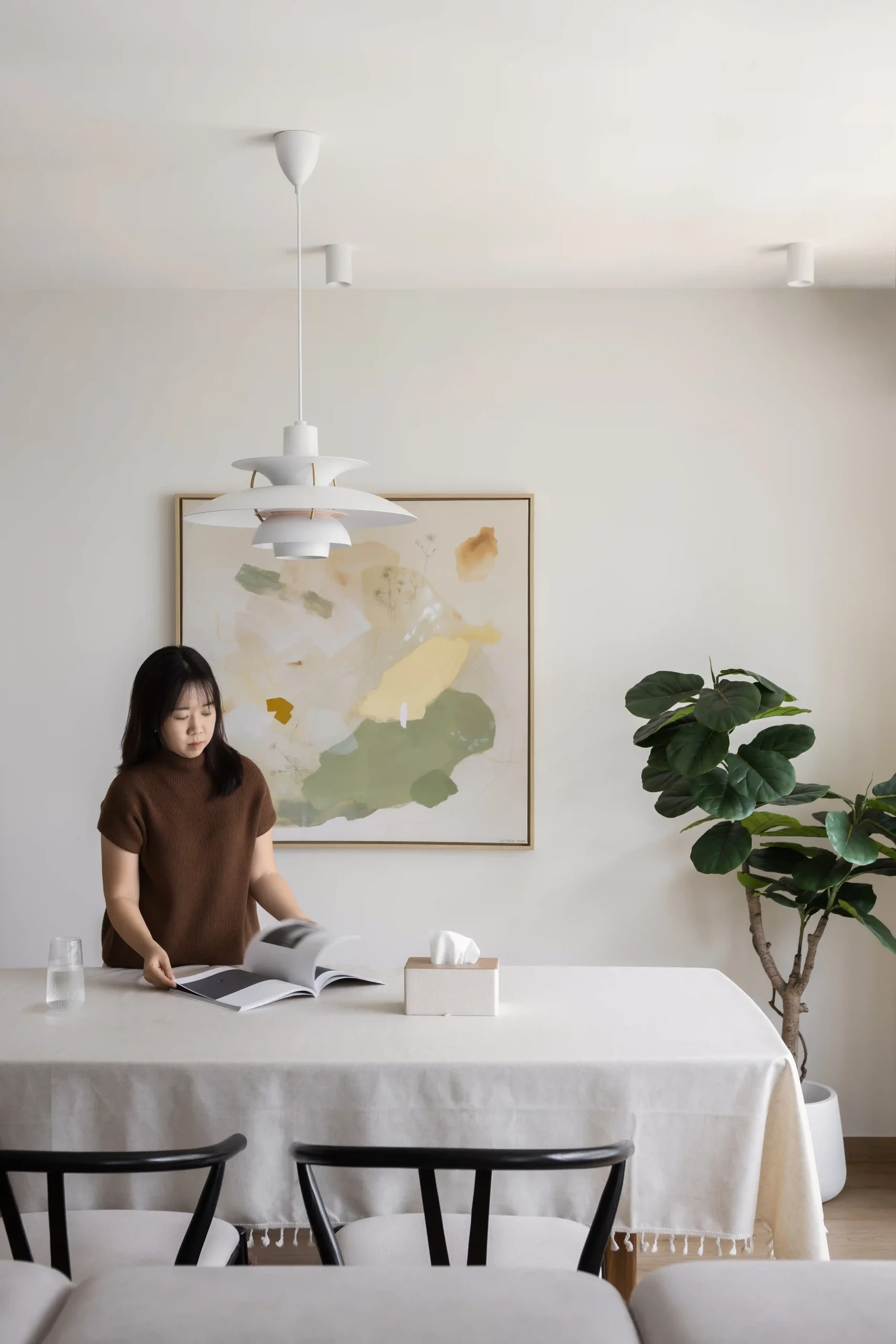 Sunlit Japandi interior design dining area with a minimalist white table, modern pendant light, and a large fiddle-leaf fig plant.