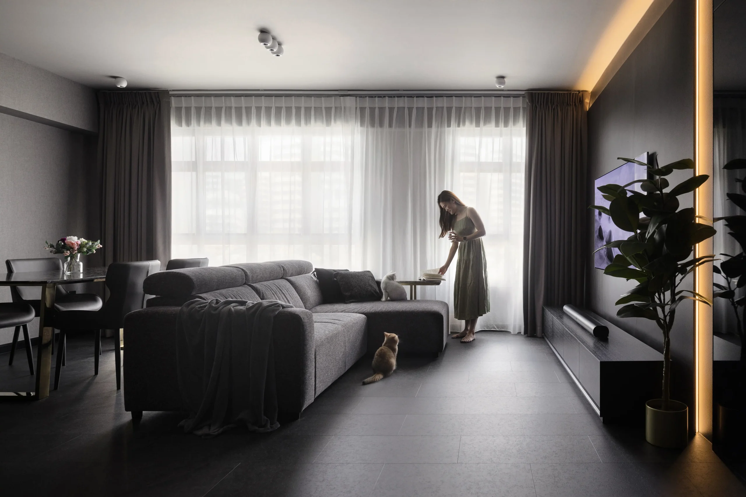 Contemporary upscale condo interior with a large charcoal sectional sofa, sheer curtains, and warm accent lighting.