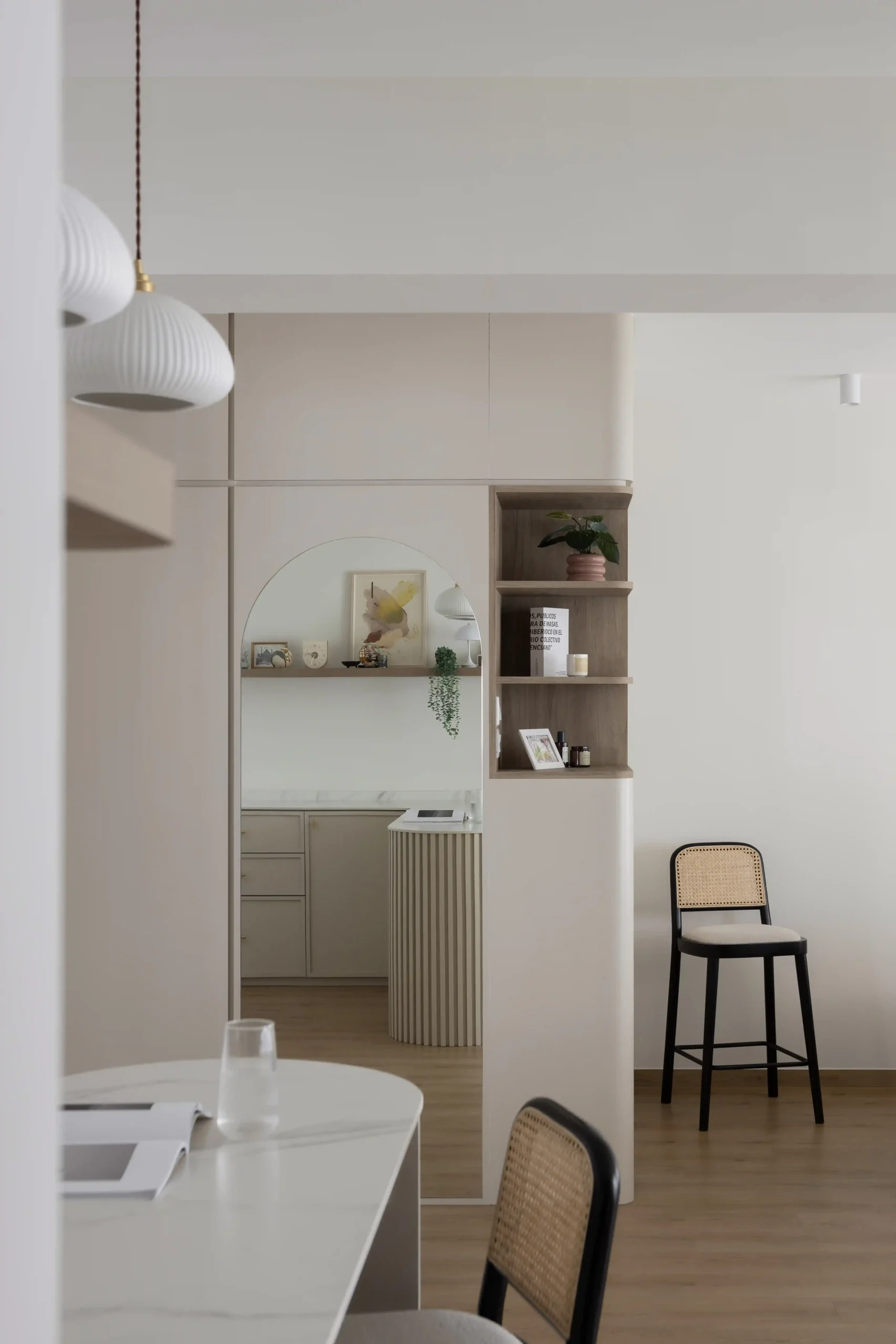 Bright Japandi interior design open-plan dining space with a view of a curved full-length mirror and wooden shelving unit.