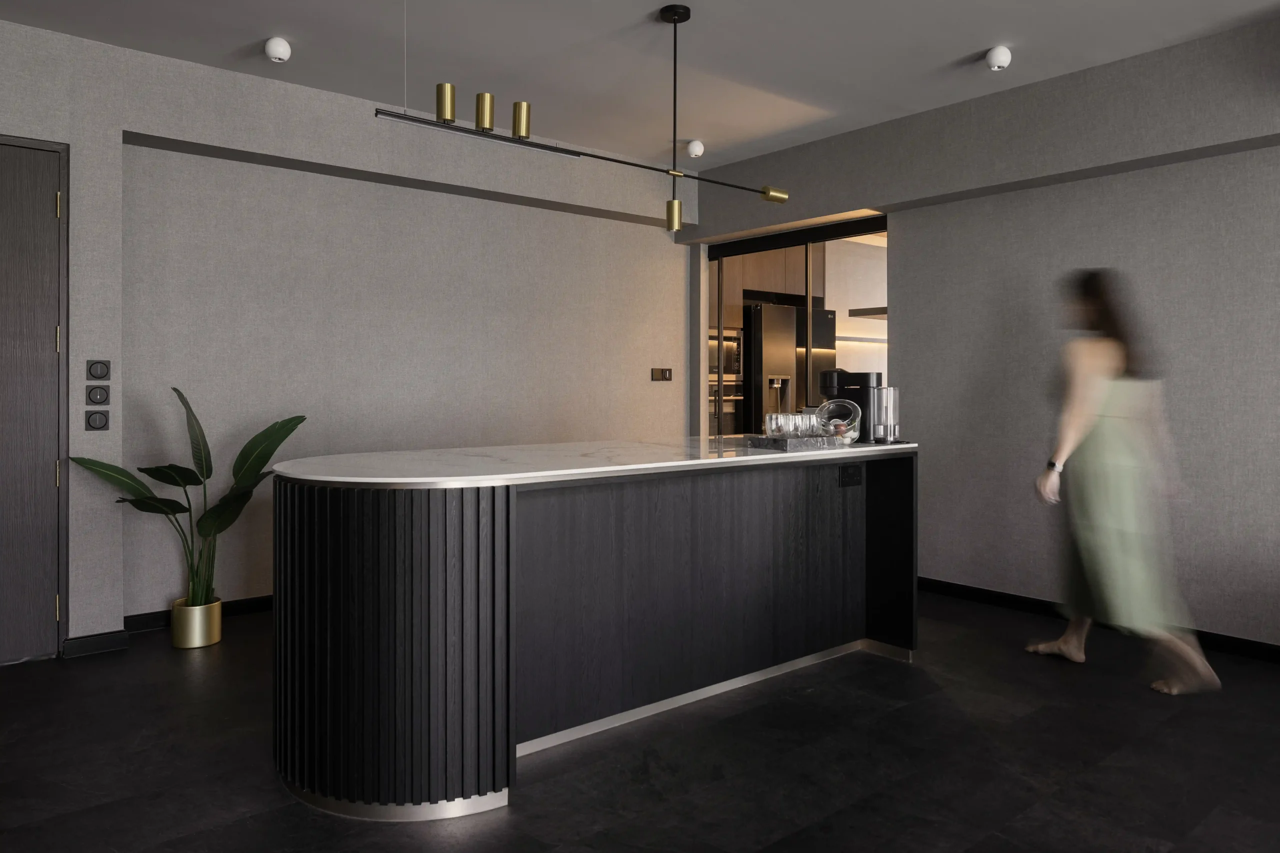 Minimalist kitchen island with a curved marble countertop and fluted dark wood paneling in a premium flat.
