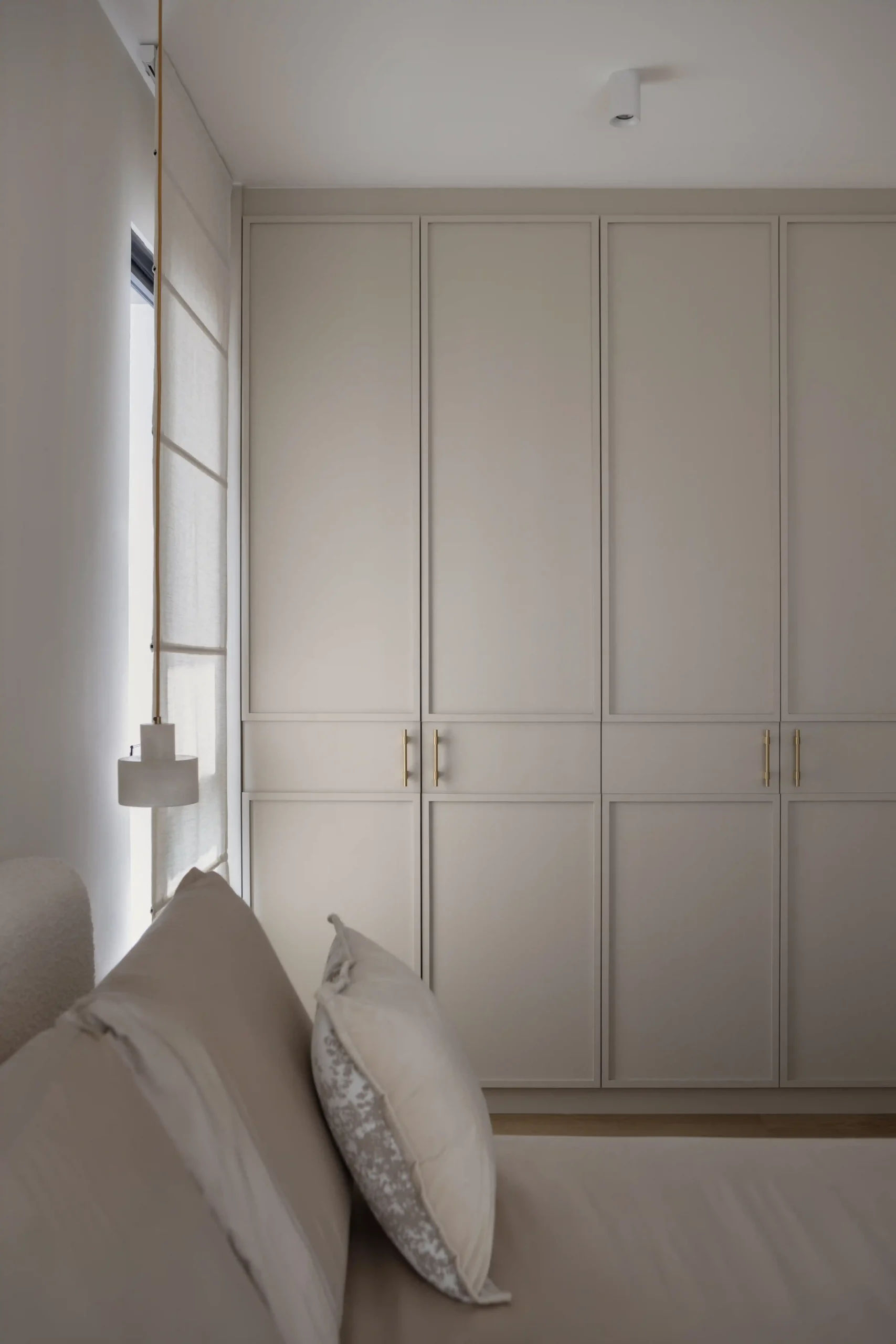 Floor-to-ceiling sleek built-in wardrobe panels in a warm neutral bedroo