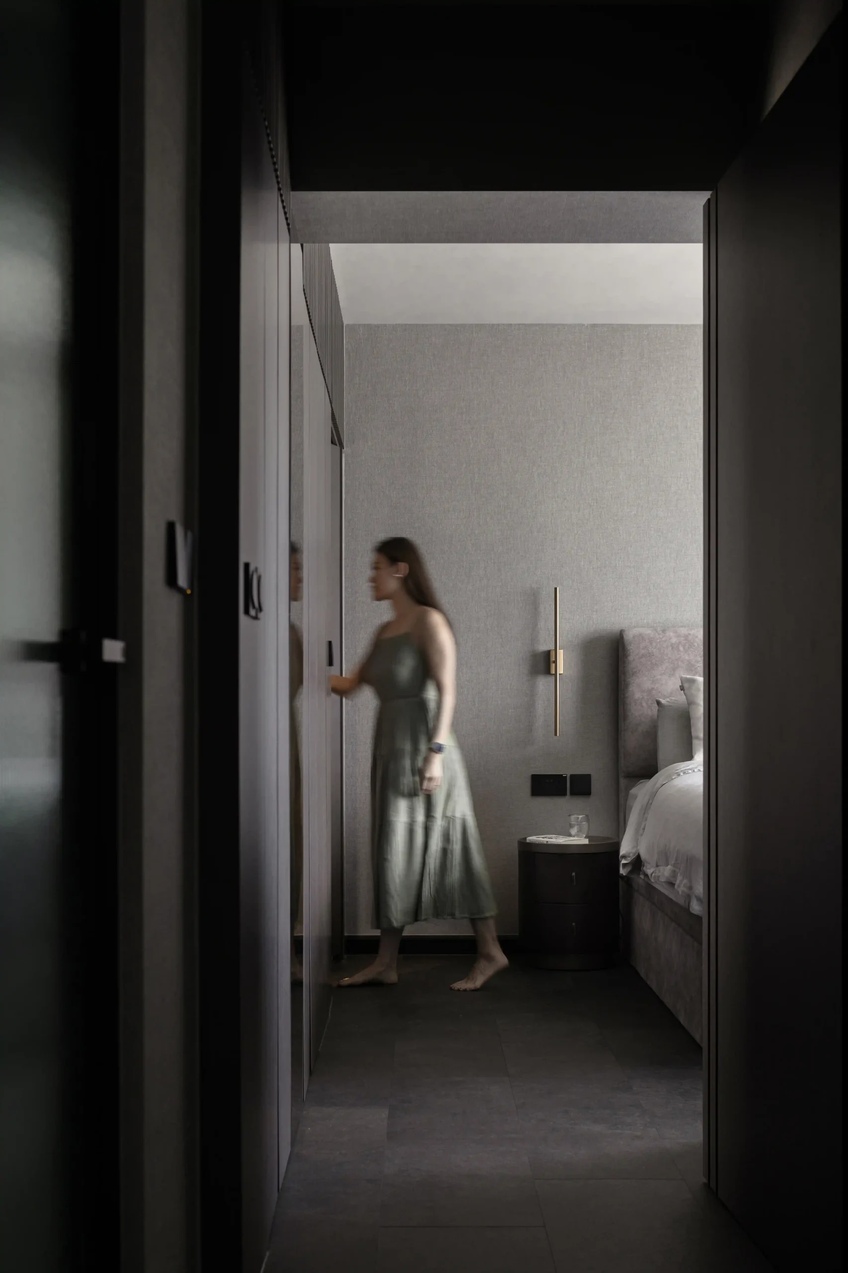 Bedroom corridor featuring floor-to-ceiling textured grey walls, brass wall sconces, and a plush grey headboard.