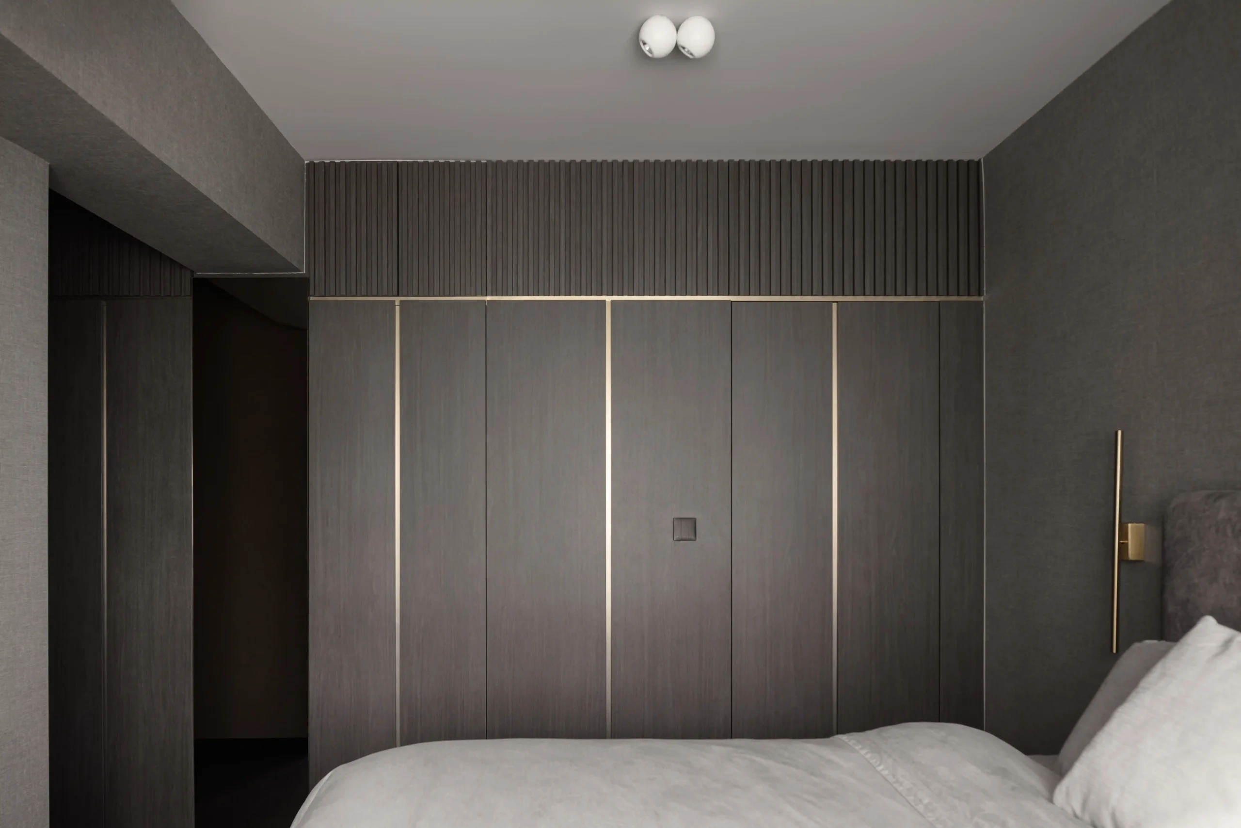 High-end master bedroom with seamless dark wood wardrobes, gold inlay details, and a fluted accent header.