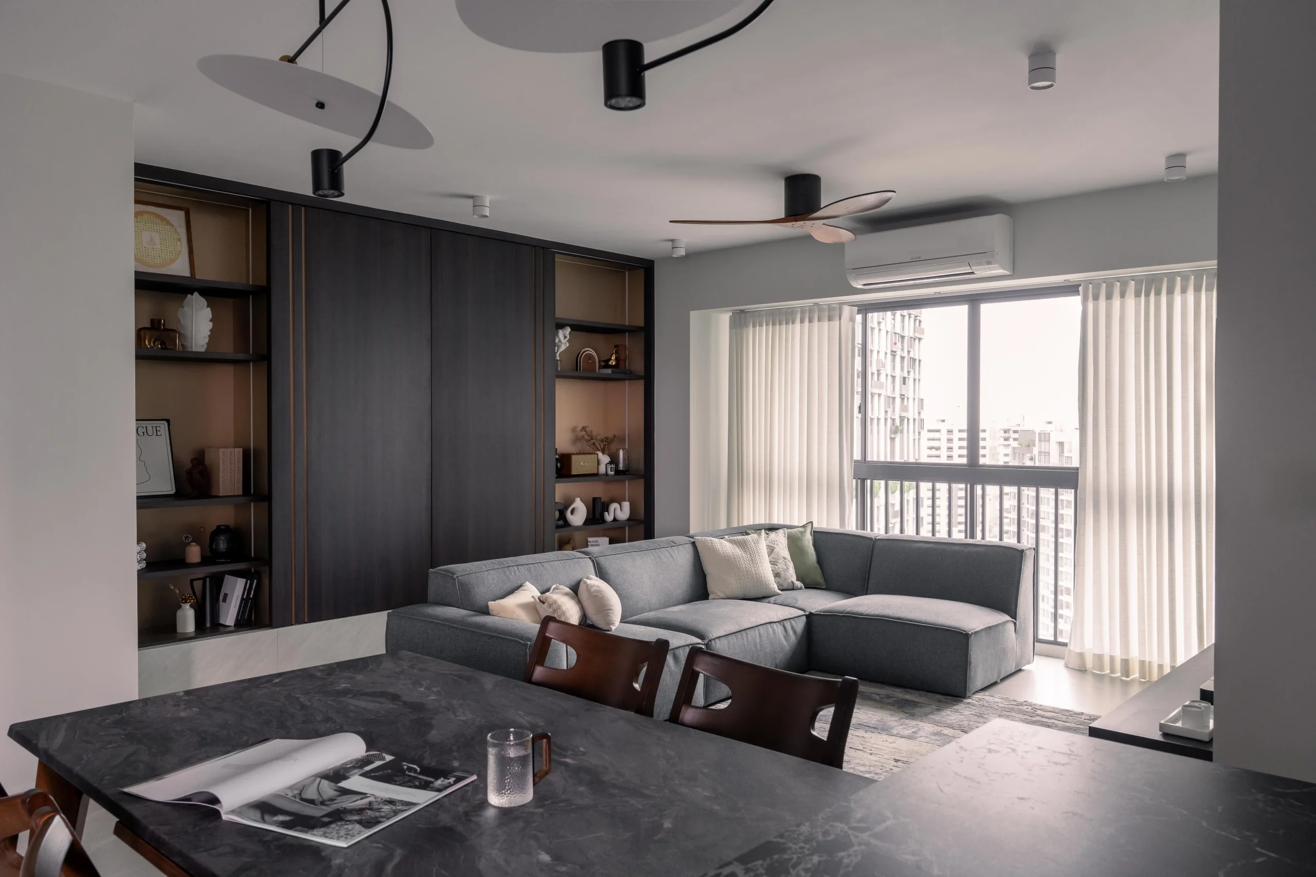 Open-plan living room with modular grey sofa, double display shelves, and city view balcony in a contemporary home interior