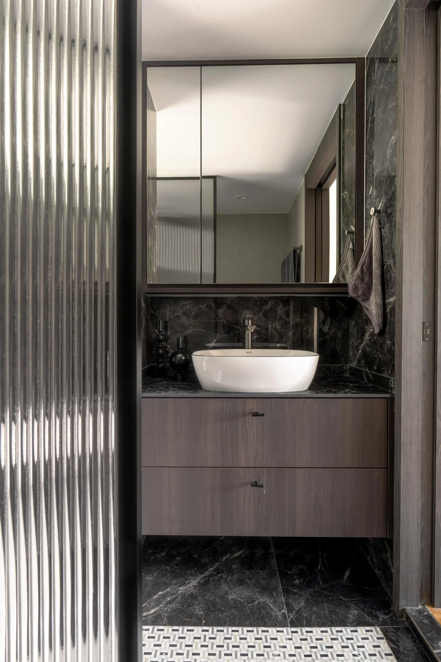 Luxury bathroom vanity with vessel sink, black marble surfaces, and ribbed glass shower partition in a sophisticated interior design