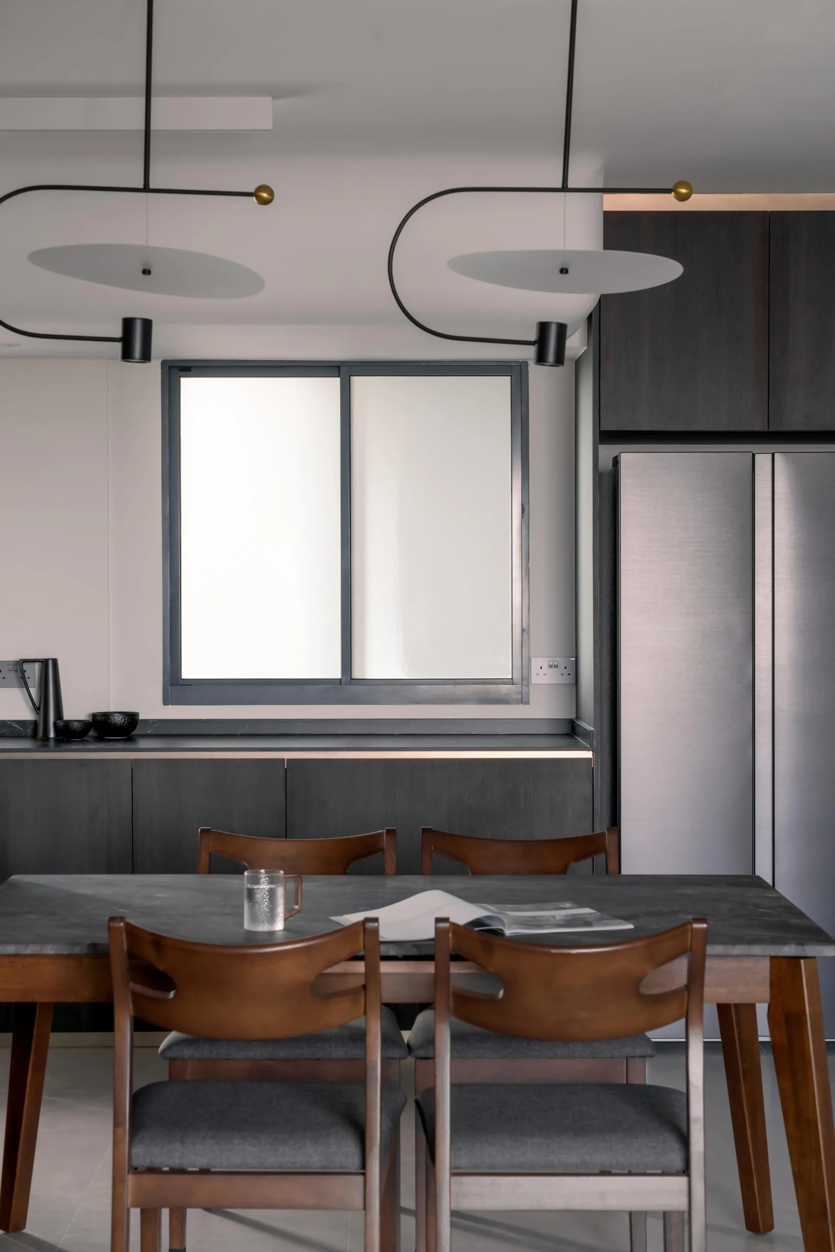 Dining area with sintered stone table, walnut chairs, and sculptural disk pendant lights in a stylish home interior