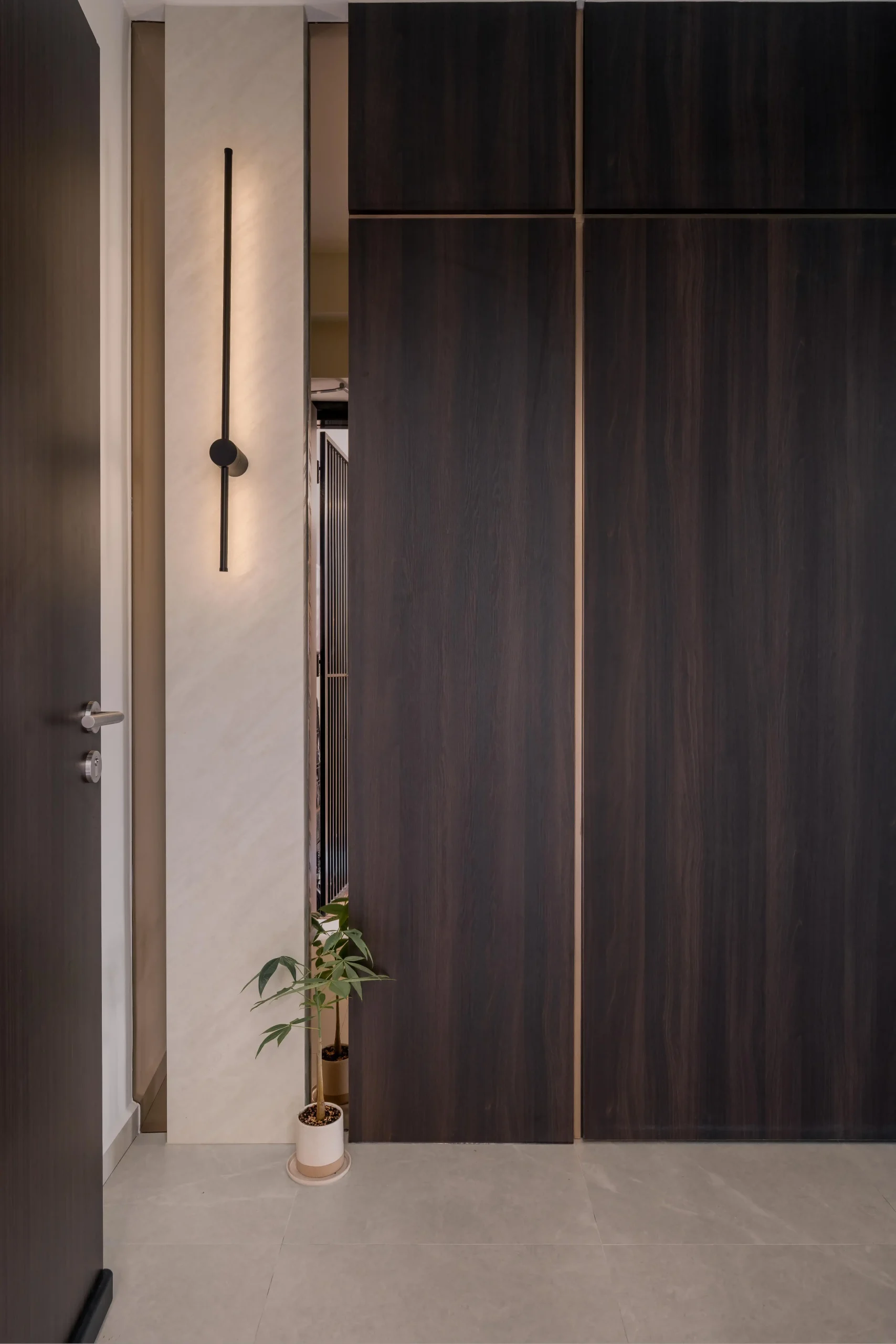 Foyer entryway with floor-to-ceiling dark wood wardrobe panels, slim linear wall sconce, and small potted plant
