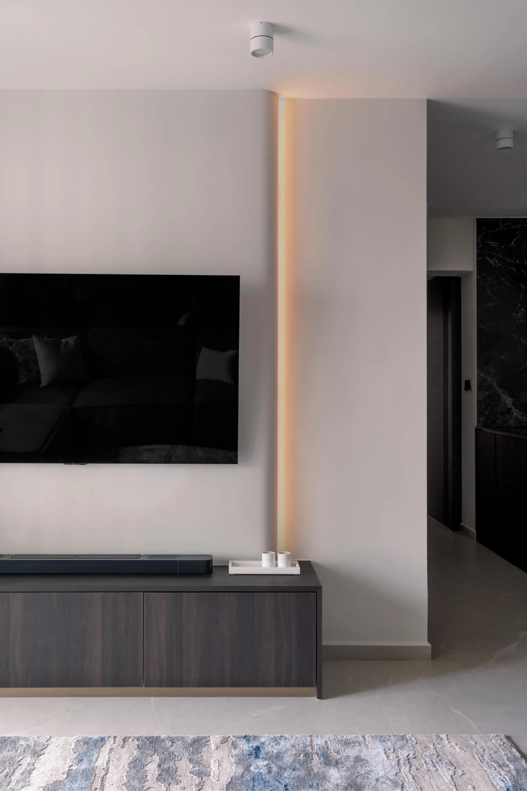 TV feature wall with recessed vertical LED cove lighting and dark wood media unit reflecting modern interior design