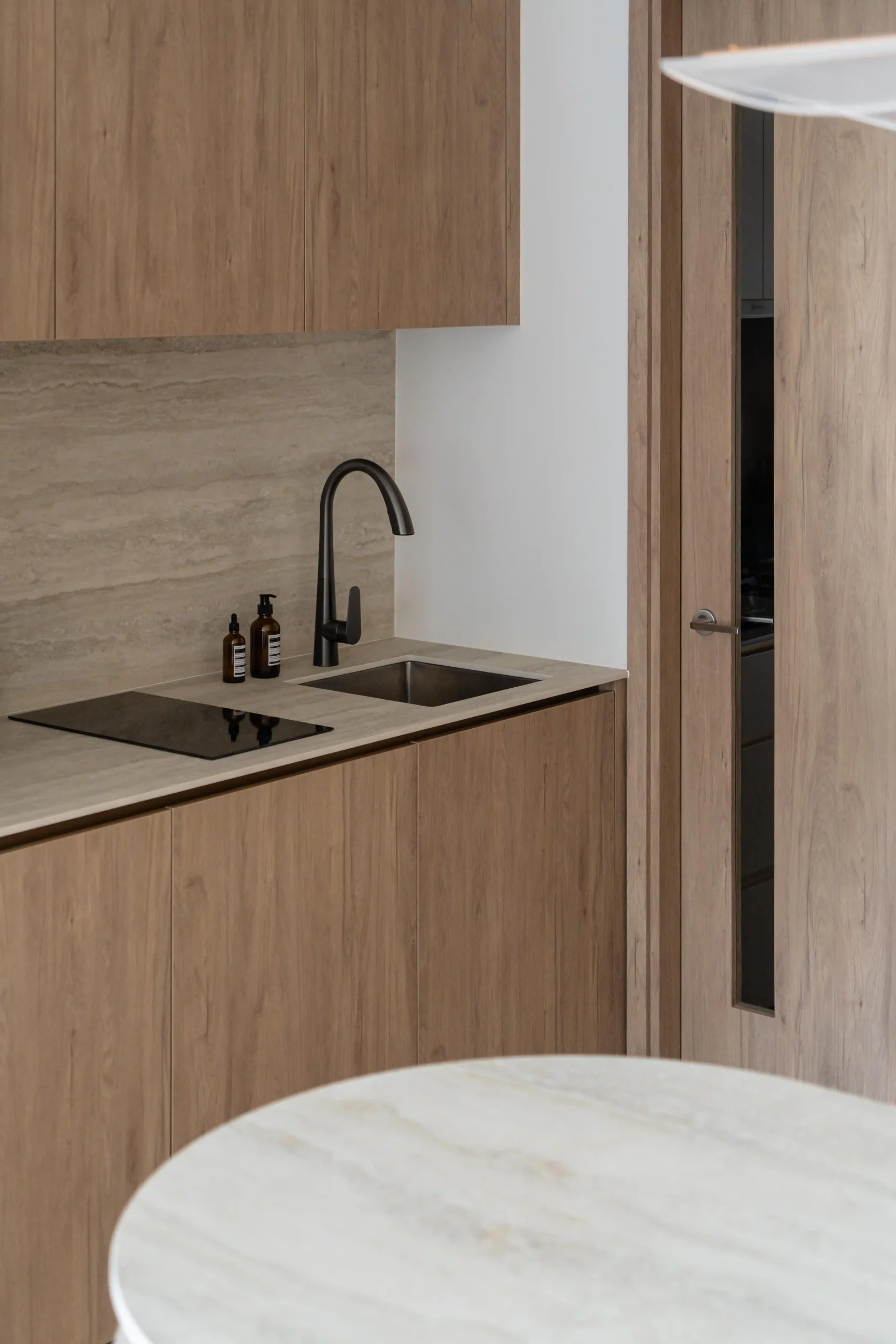 A warm japandi kitchen corner showcasing natural wood cabinets, a stone backsplash, matte black fixtures, and an induction cooktop in a clutter-free layout