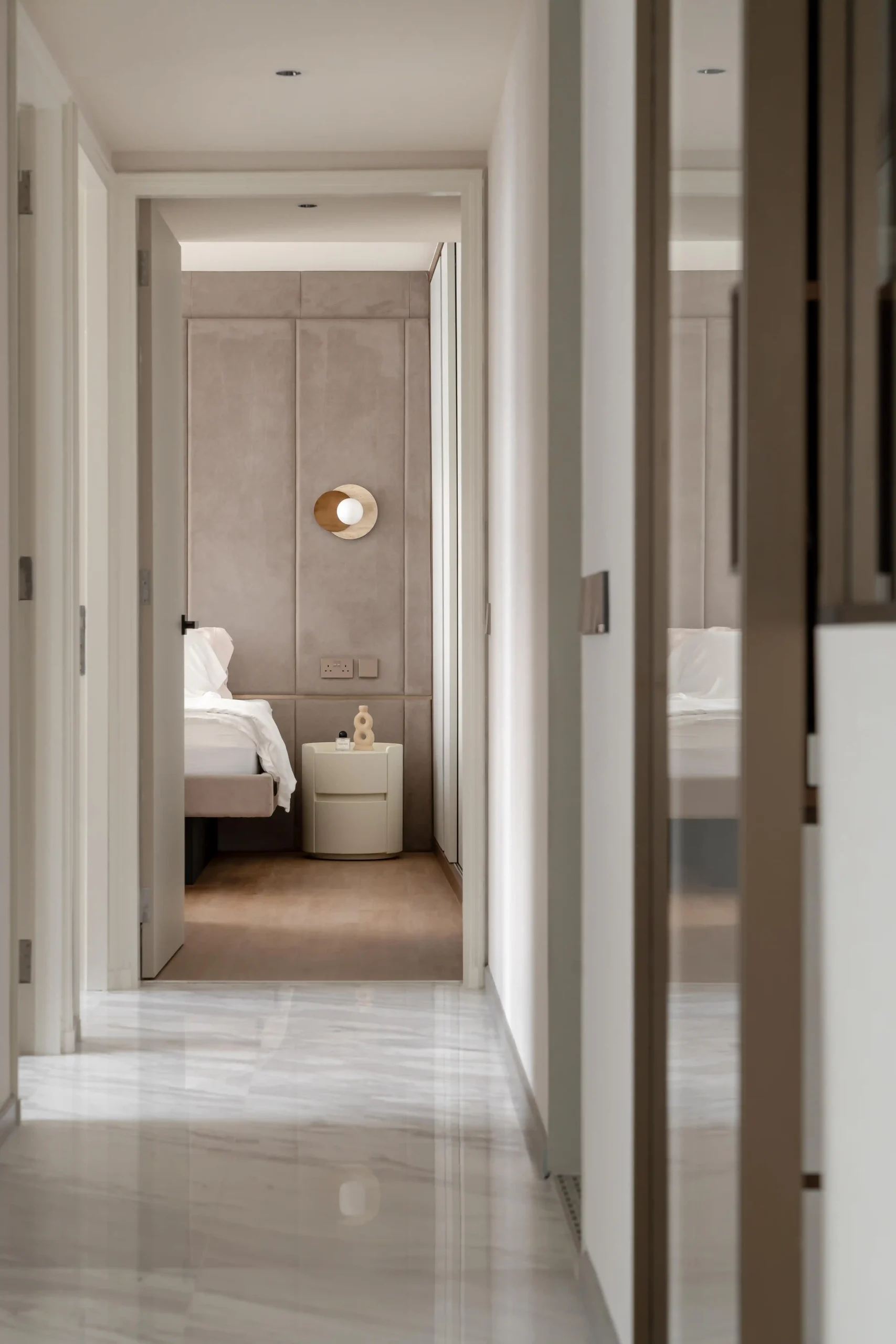 Bedroom corridor with polished marble floors and soft neutral palette leading into an upholstered headboard room with sculptural bedside table