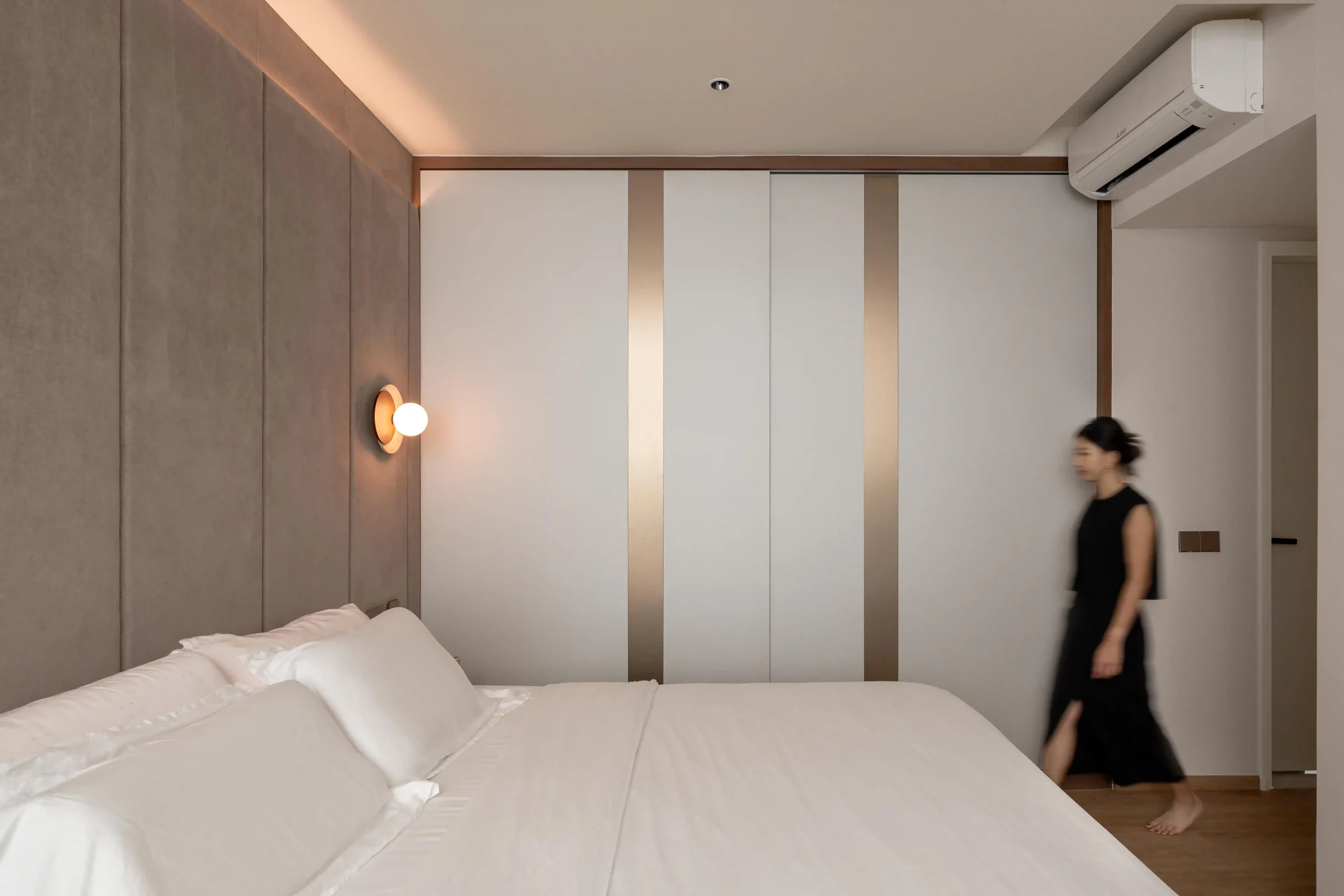 Warm ambient cove lighting over upholstered feature wall with built-in wardrobe featuring bronze inlay strips and globe wall sconce
