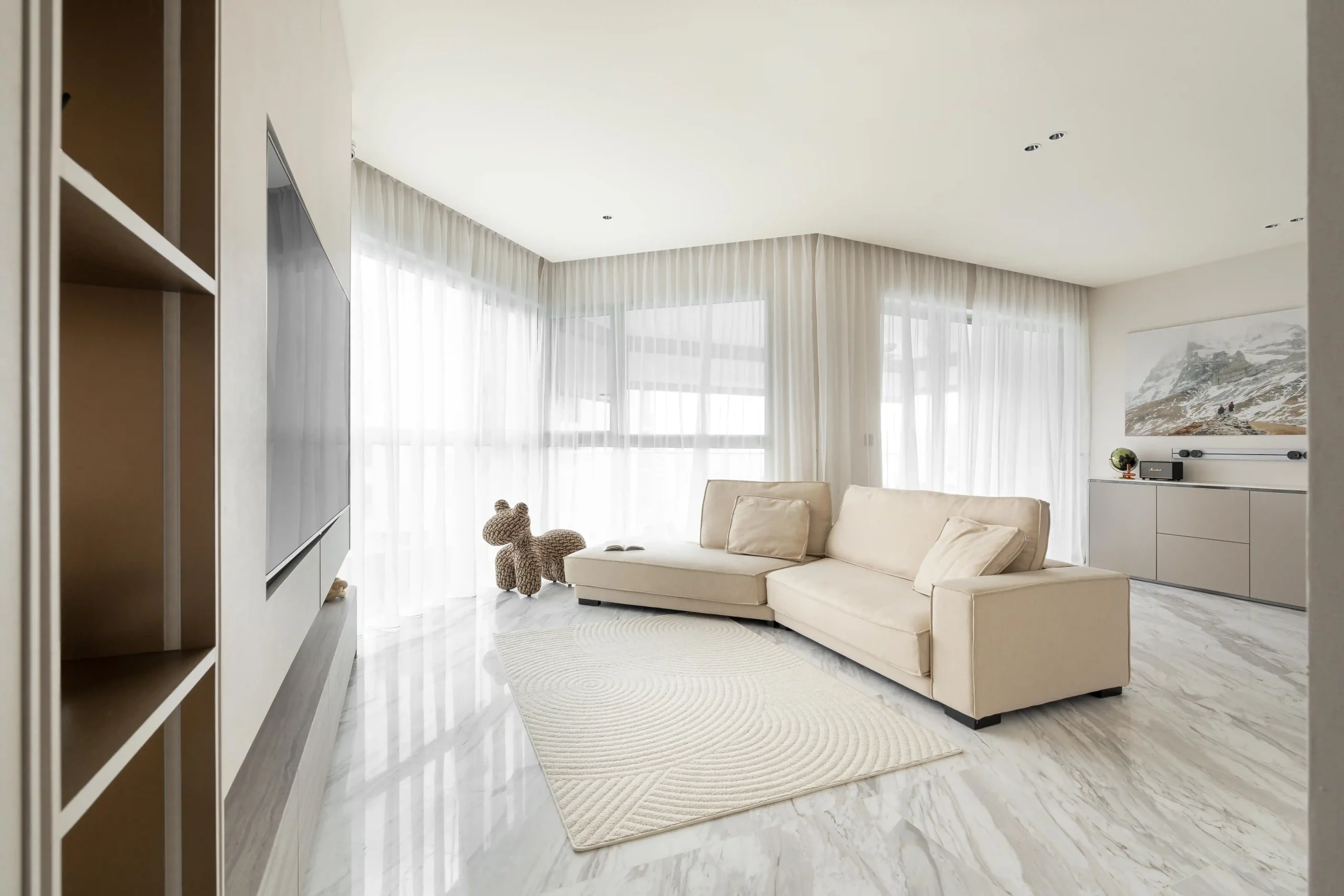 Open-plan living room with cream sectional sofa, textured circular rug, and expansive sheer-draped windows on polished marble floors