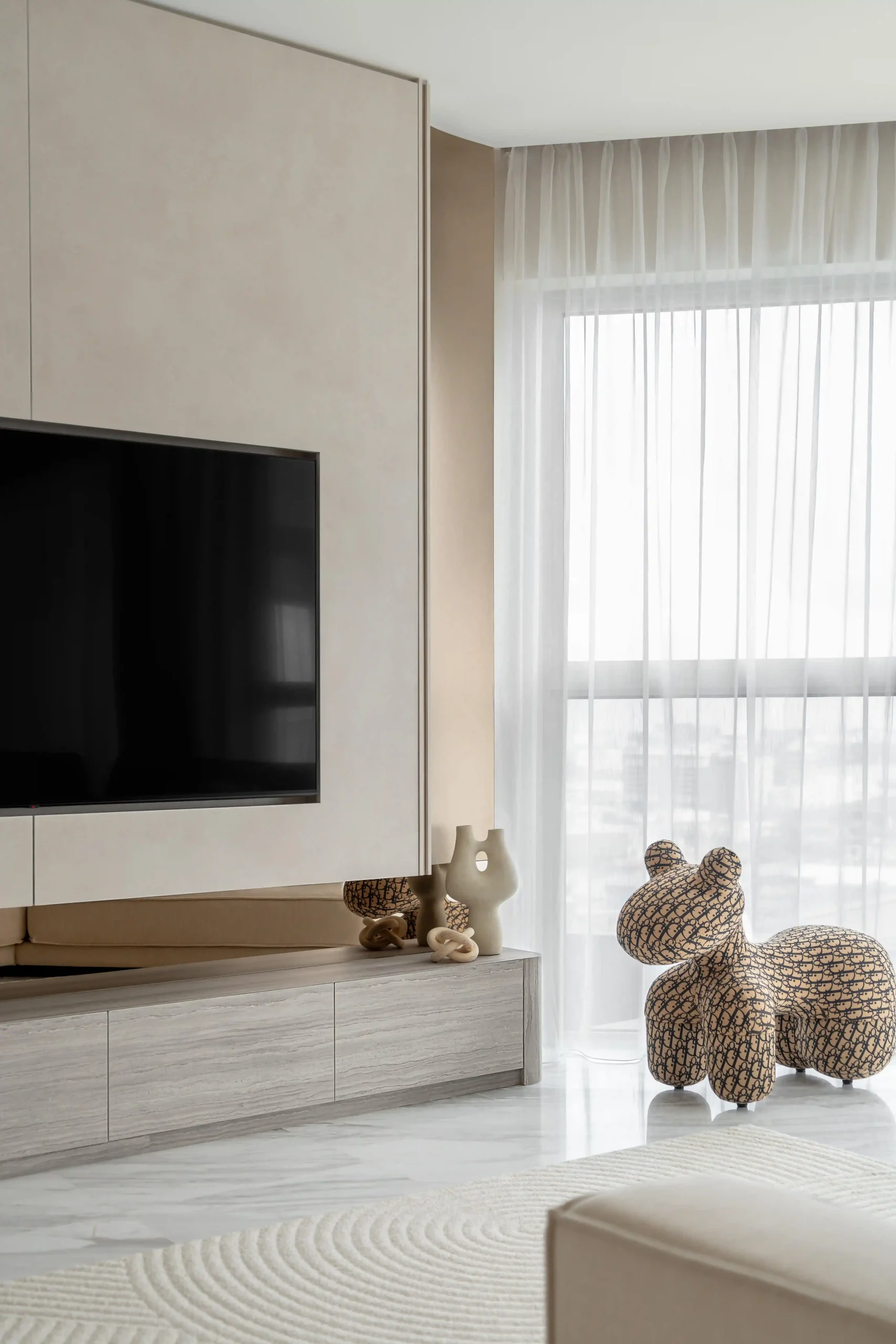 eige flush-mount TV wall panel with resort-style interior design touches — light wood media console, sculptural decor, and sheer floor-to-ceiling curtains on marble flooring