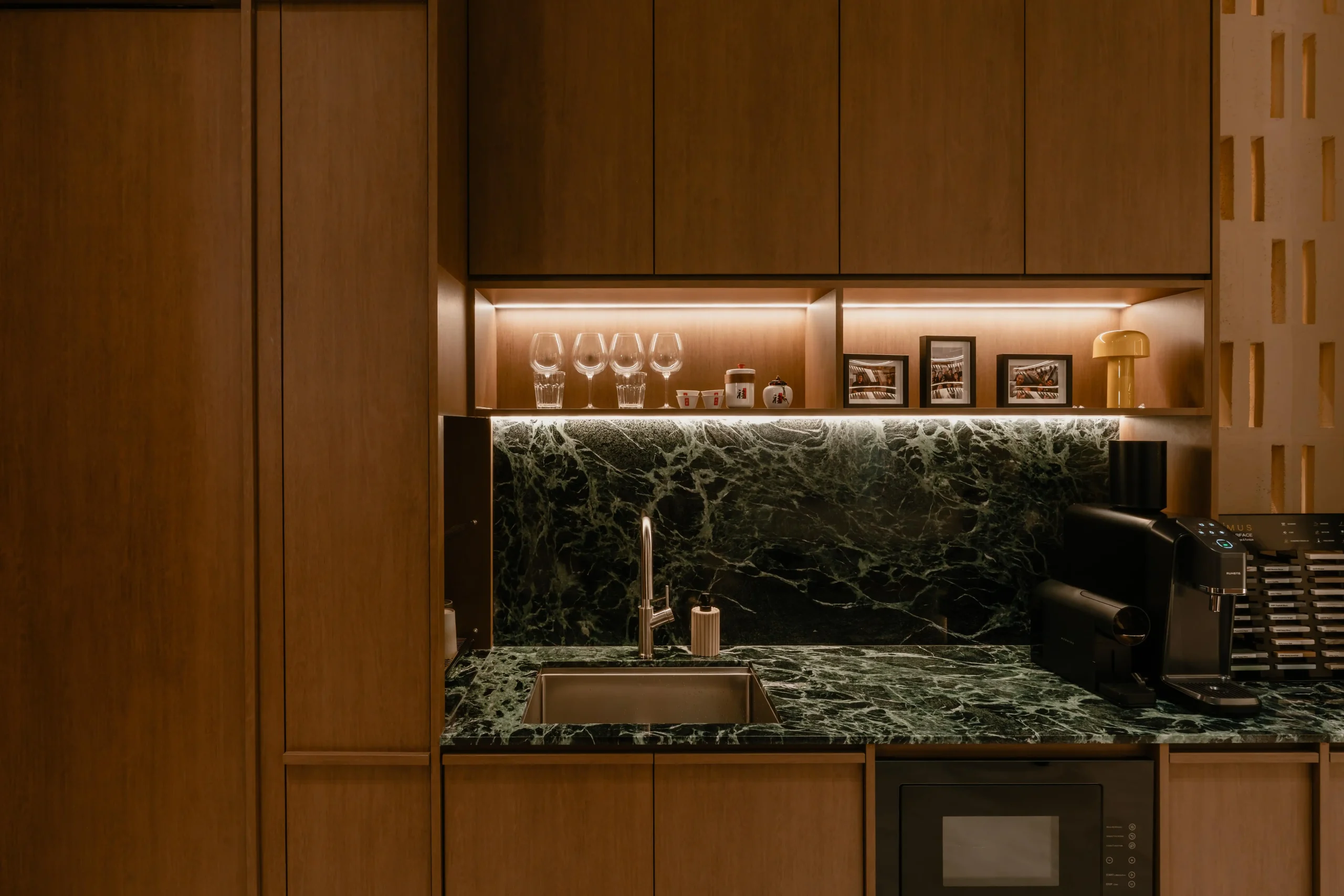 Close-up of the Sumspace Studio pantry showcasing a verde marble backsplash, integrated sink, and illuminated walnut cabinetry.