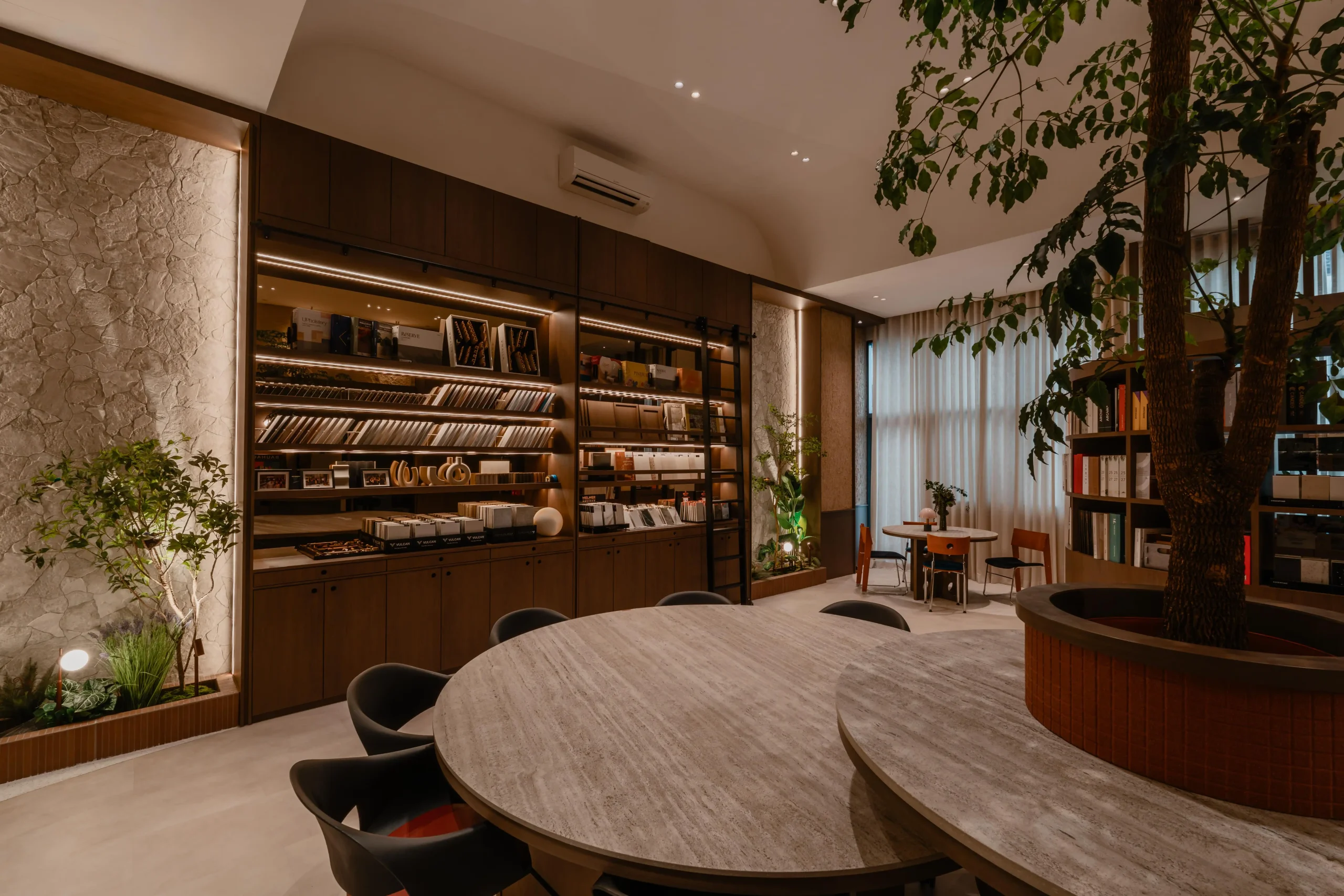 Sumspace Studio material library featuring illuminated backlit shelving, tile samples, and a large travertine table.
