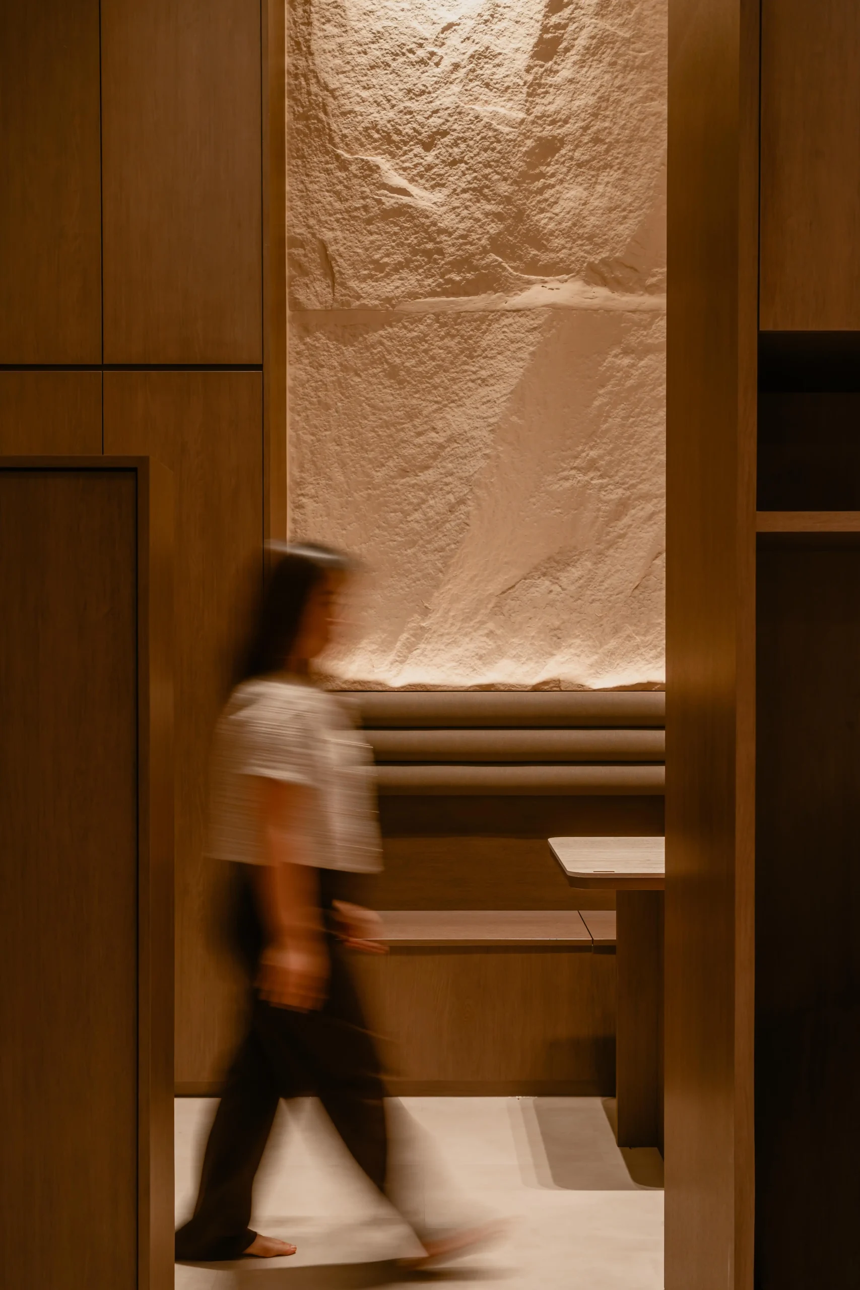 A warm, textured stone alcove with built-in bench seating hidden behind walnut partition walls.